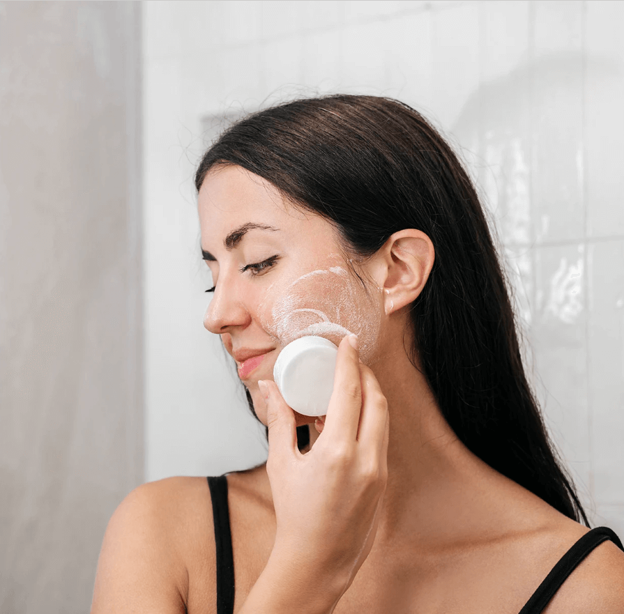 Woman gently using a mild bar facial cleanser, enriching her skin with a natural wash in a bright bathroom.